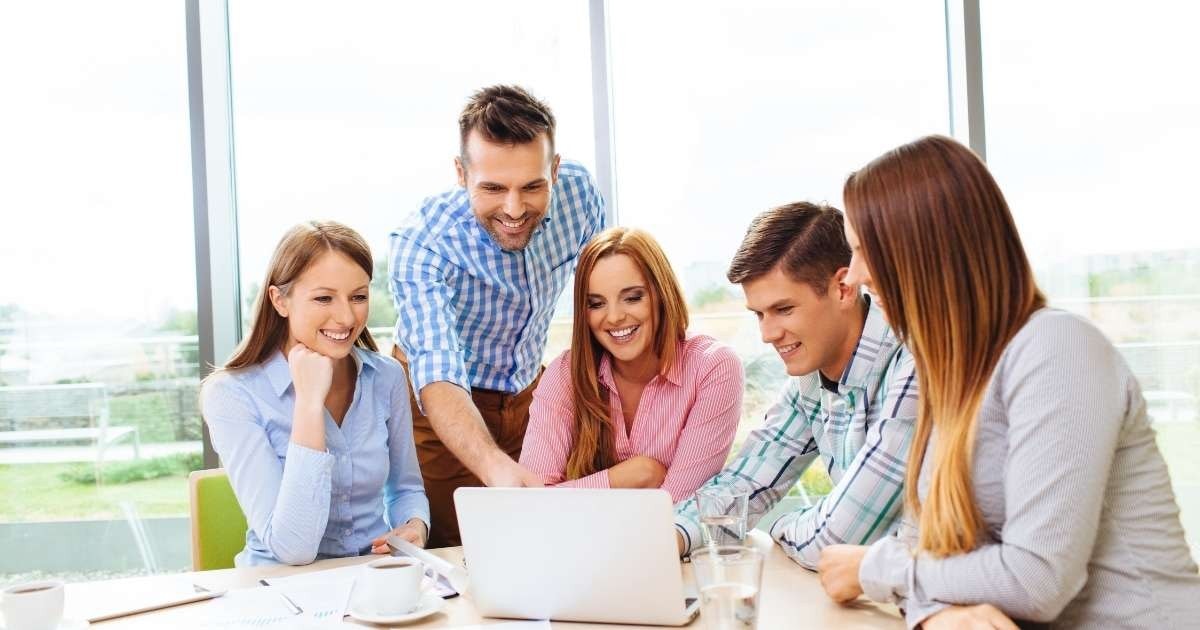 İki erkek ve bir kadından oluşan üç kişilik bir grup beyaz bir dizüstü bilgisayarın etrafında oturmaktadır. Kadın elini çenesine dayamış, gülümsüyor. Soldaki adam dikkatle dizüstü bilgisayara bakmakta, sağdaki adam ise ona gülümsemektedir. Önlerindeki masanın üzerinde bir bardak sıvı var. Dizüstü bilgisayar açık ve ekranı parlak bir şekilde aydınlatılmış. Kadının uzun, parlak kızıl saçları vardır. Soldaki adam mavi bir gömlek, sağdaki adam ise yeşil bir gömlek giyiyor. Beyaz duvarları ve ahşap zemini olan bir odadalar.