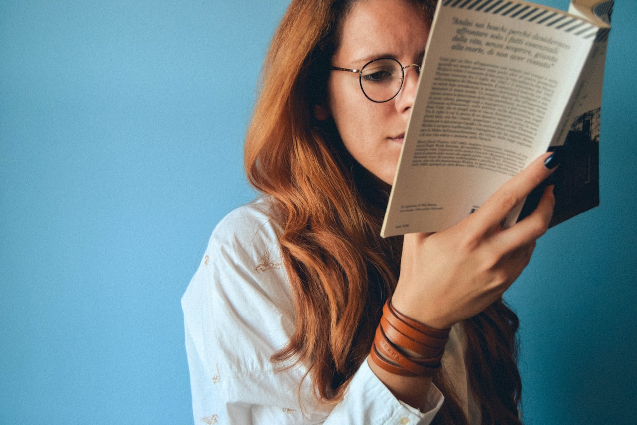 Resimde dikkatle kitap okuyan bir kadın görülüyor. Uzun, kızıl saçları var ve iki kahverengi deri bilezikle beyaz bir gömlek giyiyor. Yüzü yakın plandadır ve izleyicinin gözlerini ayrıntılı olarak görmesini sağlar. Sağında, yakın planda, karmaşık desenleri olan bir bilezik var. Arka plan bulanıklaştırılarak odağın kadın üzerinde kalması sağlanmış. Görüntü üstten çekilmiş ve izleyicinin kadının ve çevresinin genel bir görünümünü elde etmesini sağlıyor. Yüzünde ciddi bir ifade var, sanki tamamen okumaya dalmış gibi.