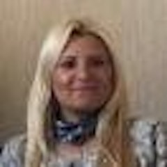 Bu, geniş ve ışıltılı bir gülümsemeye sahip bir kadının yakın plan görüntüsüdür. Gözleri kapalı bir şekilde doğrudan kameraya bakıyor ve dişleri dişlek bir sırıtışla görünüyor. Yanakları hafifçe pembe ve yüzü neşe dolu. Saçları geriye çekilmiş ve yüzünden uzakta ve gözleri parlak mavi. Dudakları hafifçe ayrılmış ve sol yanağında hafif bir gamze var. Rahat ve memnun görünüyor, vücut dili sakin ve mutlu bir his veriyor. Bakışları davetkâr ve sıcak, açıklık ve kabullenme havası yansıtıyor.