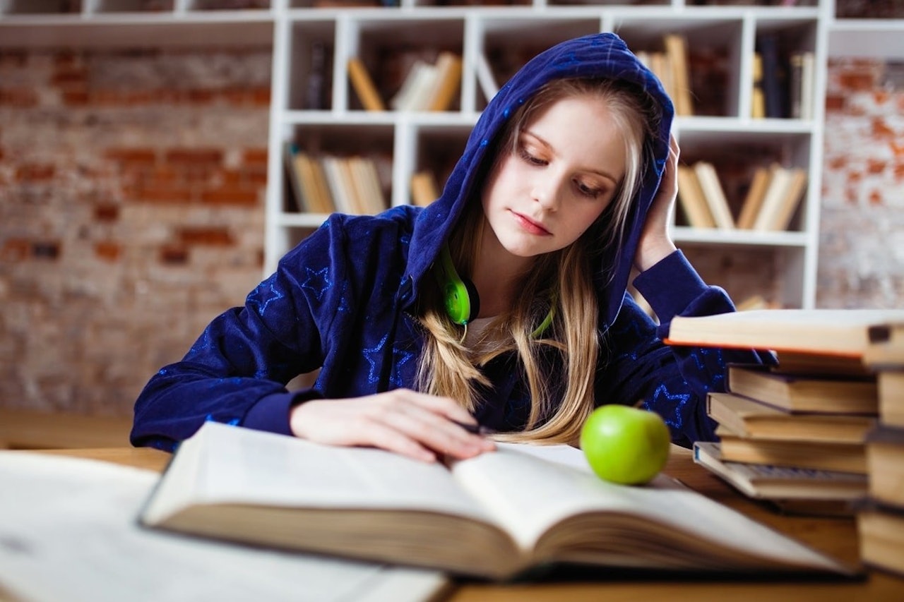Genç bir kız masada oturmuş, dikkatini önündeki kitaplara ve yeşil elmaya vermiş. Kızın üzerinde kapüşonlu bir tişört var ve elleri kitaplardan birinin açık sayfaları üzerinde dururken görülüyor. Arka planda bulanık bir klavye görüntüsü ve yeşil bir elmanın yakın çekiminin yanı sıra bir kişinin elinin, kolunun, başının ve bir masanın bulanık bir resmi var. Kızın etrafı kitaplarla çevrili ve dikkati elindeki işe odaklanmış görünüyor. Konsantre oluyor ve kitaplar ve elma çalışması için teşvik edici bir ortam sağlıyor.