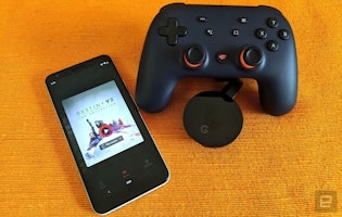 Siyah bir oyun kumandası, siyah ve turuncu düğmeli bir cep telefonunun yanına yerleştirilmiştir. Kumandanın yüzeyinde dairesel bir nesne bulunmaktadır. Telefon ekranında siyah ve turuncu bir çarpı işareti olan bir oyun görüntülenmektedir. Görüntü, oyunu ve kumandayı ayrıntılı bir şekilde gösteren cihazın yakın çekimidir. Kumanda, yön düğmeleri, bir joystick ve haç şeklinde bir düğme ile gri ve beyaz bir gövdeye sahiptir. Telefonun siyah bir gövdesi ve devam etmekte olan bir oyunu gösteren bir ekranı var. Sahne siyah oyun kumandası, cep telefonu ve ekrandaki oyundan oluşuyor.