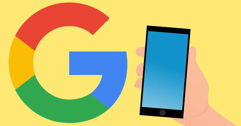 Mavi ekranlı bir cep telefonu tutan bir elin yakın plan görüntüsü. Telefonda renkli bir G harfi görülüyor. Telefon sol elle tutuluyor, sağ elin parmakları ekrana dokunuyor. Cihaz dikdörtgen şeklindedir, mavi ve yeşil bir arka planı vardır. Telefonun üst kısmı alt kısmından biraz daha yüksektir. Cep telefonunun alt ve yan kısımlarında açık mavi bir kenarlık vardır ve hafif eğimlidir. Görüntü hafif yüksek bir açıdan çekilmiştir.