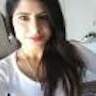 Uzun kumral saçlı genç bir kadın telefonuyla selfie çekiyor. Yüzünde parlak bir gülümseme var ve gözleri neşe içinde kapalı. Beyaz bir tişört giymiş ve halka küpeler takmış. Kolunu uzatmış, telefonu elinde, anı yakalamaya hazır. Kamera açısı hafif yukarıdan, fotoğrafa hafif açılı bir perspektif veriyor. Arka plan bulanıklaştırılarak odağın kadında kalması sağlanmış. Kadının pozu rahat ve eğleniyor gibi görünüyor. Bu fotoğraf selfie çekmenin keyfini mükemmel bir şekilde yansıtıyor.