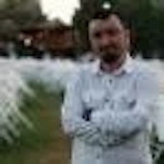 Bir adam kollarını kavuşturmuş, siyah bir tişört ve kot pantolon giymiş halde duruyor. Başı hafifçe yana eğiktir ve yüz ifadesi ciddidir. Kısa siyah saçları ve kesilmiş sakalı var. Kollarını göğsünün önünde kavuşturmuş ve başının üzerinde bir çift koyu renk güneş gözlüğü duruyor. Arka plan düz beyaz bir duvardır ve adam yandan gelen parlak bir ışıkla aydınlatılmıştır. Kadrajın ortasında kendinden emin bir şekilde durmakta ve uzaklara bakmaktadır. Duruşu ve ifadesi kararlılık ve güç gösteriyor.