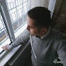 Adam pencerenin önünde durmuş, dışarıdaki dünyaya bakmaktadır. Derin düşüncelere dalmış gibi görünüyor, bakışları uzak ve ifadesi ciddi. Elleri önünde kenetlenmiş, vücudu ve duruşu bir tefekkür hissi veriyor. Güneş pırıl pırıl parlıyor ve gökyüzü masmavi, uzaklarda beyaz bulutlar uçuşuyor. Manzarayı çerçeveleyen pencere, dikey ve yatay çizgileriyle belirgin ve davetkâr bir çerçeve oluşturuyor. Adam huzurlu bir atmosferle çevrili ve onun varlığı sahnenin güzelliğine katkıda bulunuyor.