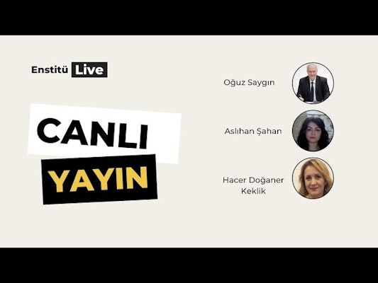Bir grup insan bir odada daire şeklinde toplanmıştır. Çemberin ortasında takım elbise giymiş bir adam göze çarpmaktadır. Ciddi bir ifadeyle kameradan uzağa bakmaktadır. Adamın solunda bir kadın kameraya gülümsemektedir. Koyu renk saçları var ve açık renkli bir elbise giyiyor. Adamın sağında, kollarını kavuşturmuş bir başka kadın duruyor. O da koyu renk saçlı ve kameradan uzağa bakıyor gibi görünüyor.