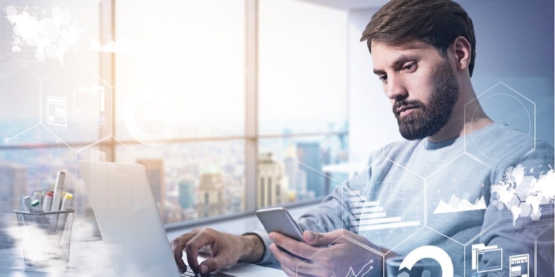 Sakallı ve gözlüklü bir adam masa başında oturmuş, dizüstü bilgisayar ve cep telefonu kullanıyor. Dikkatle telefonuna bakıyor gibi görünürken diğer eli dizüstü bilgisayarın klavyesinde duruyor. Yanında bir sepet dolusu kalem ve masanın üzerinde bir fincan duruyor. Yüzü yakın plandadır ve kararlı bir ifadesi vardır. Görevine konsantre olmuş gibi görünüyor ve odağı elindeki telefonda.