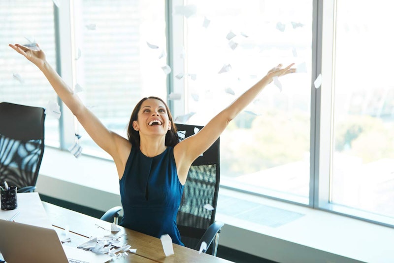 Bir kadın masa başında oturmuş, havaya kâğıt atmaktadır. Mavi bir elbise giymiş ve etrafında büyük bir kâğıt yığını var. Yüzü parlak bir gülümsemeyle aydınlanmış ve gözleri gülerek kapanmış. Kollarını uzatmış ve bir eliyle havada bir kağıt parçası tutuyor. Arkasında bir dizüstü bilgisayar, yan tarafında ise kalemlerle dolu siyah bir fincan var. Görüntü biraz bulanık ama arka planda bir sandalyenin ayakları seçilebiliyor. Bu kadın bir sevinç ve kutlama anının ortasında, elindeki kağıtları havaya fırlatıyor gibi görünüyor.