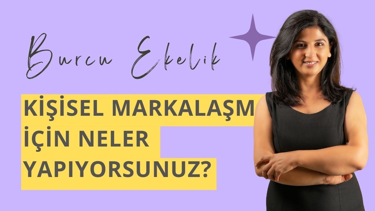 Siyah elbiseli bir kadın kollarını kavuşturmuş, göğsünde mor bir yıldızla duruyor. Yüzünü çerçeveleyen koyu renk saçlarıyla gülümsüyor. Arkasında büyük Y harfi olan sarı ve siyah bir tabela var. Her iki yanında siyah harflerle mor zeminler var. Sağ eli dirseğine dokunuyor.