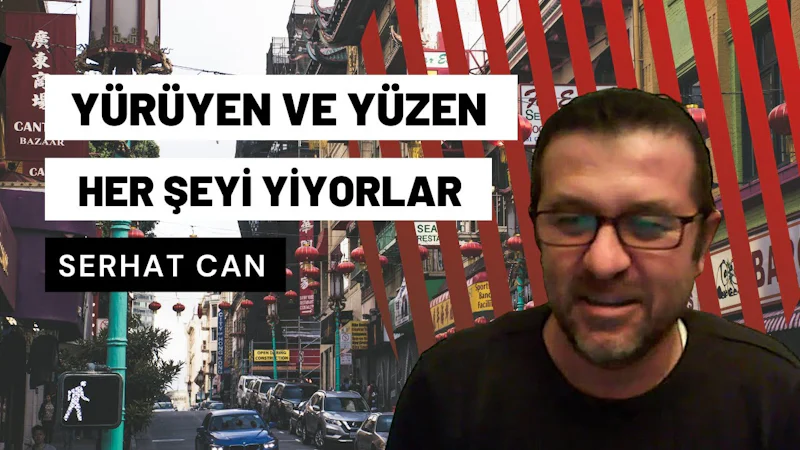 Çerçevenin ortasında, beyaz metinli siyah bir arka planın önünde duran siyah gömlekli bir adam görülüyor. Gözlük takıyor ve yüzünde ciddi bir ifade var. Resmin alt kısmında, ön camında birkaç delik olan mavi bir araba görülüyor. Adamın sağında, ayrıntılı bir metin ve renkli bir arka plan içeren bir tabelanın yakın çekimi görülüyor. Adamın solunda ise beyaz arka planlı, kırmızı ve siyah metinli bir başka tabelanın yakın çekimi görülüyor. Siyah gömlekli adam doğrudan kameraya bakıyor gibi görünüyor.
