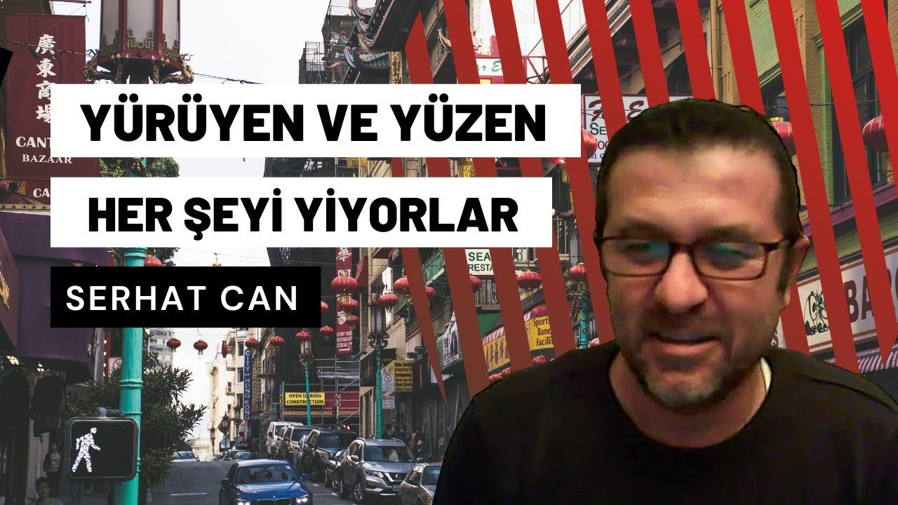 Çerçevenin ortasında, beyaz metinli siyah bir arka planın önünde duran siyah gömlekli bir adam görülüyor. Gözlük takıyor ve yüzünde ciddi bir ifade var. Resmin alt kısmında, ön camında birkaç delik olan mavi bir araba görülüyor. Adamın sağında, ayrıntılı bir metin ve renkli bir arka plan içeren bir tabelanın yakın çekimi görülüyor. Adamın solunda ise beyaz arka planlı, kırmızı ve siyah metinli bir başka tabelanın yakın çekimi görülüyor. Siyah gömlekli adam doğrudan kameraya bakıyor gibi görünüyor.