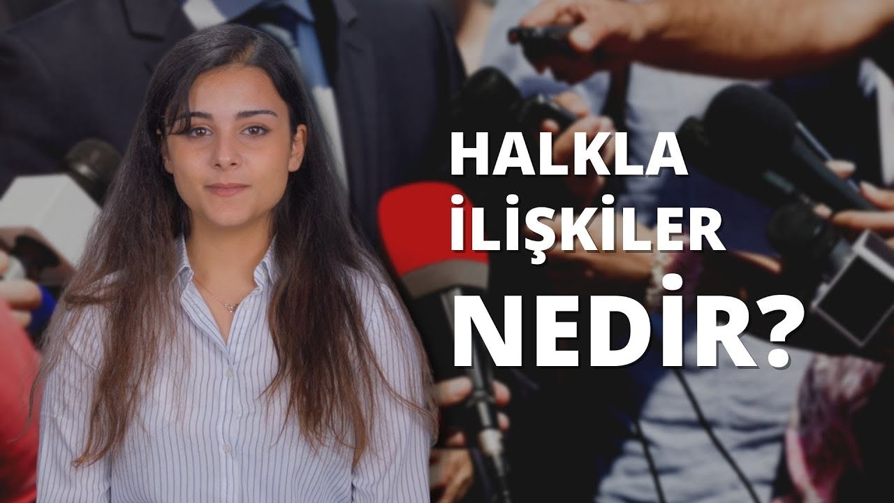 Uzun siyah saçları sırtından aşağı dökülen bir kadın mikrofonun önünde duruyor. Yüzünde parlak ve kendinden emin bir ifade var. Kollarını vücudunun yanında rahat bir pozisyonda tutuyor ve ellerini önünde kavuşturmuş. Siyah bir gömlek giyiyor ve arka planda sağ elinde bulanık bir nesne görülebiliyor. İçinde durduğu oda loş bir şekilde aydınlatılmış ve önünde durduğu mikrofon sıcak ve davetkâr bir atmosfer yansıtıyor. Bu, mesajını dünyayla paylaşmaya hazır, kendinden emin ve dengeli bir kadının görüntüsüdür.