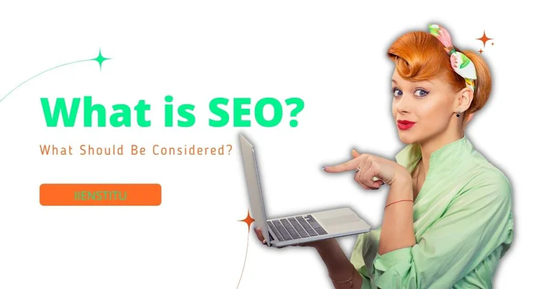 A woman wearing a green shirt is holding a laptop in her hands. She has short, red hair with a black bow in it. There is a cigarette in her right hand. The laptop has a black cover and a white screen. On the left side of the woman, there is an orange rectangular sign with green text. She has a focused expression and is looking directly at the laptop. Her left hand is pointing to the laptop while her right hand is holding it steady. The laptop is positioned in such a way that the viewer can see the woman's face.