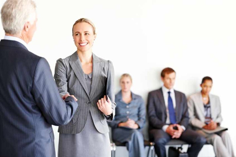 Takım elbiseli bir kadın ve bir adam karşı karşıya durmuş el sıkışmaktadır. Adam gri bir takım elbise giymiş ve mavi bir kravat takmıştır. Kadın sol elini sağ kolunun üzerine koymuş. Her ikisinin de yüzü odaklanmış ve iletişim kuruyor gibi görünüyorlar. Arka plan net değil ama sağ alt köşede siyah bir nesnenin bulanık bir görüntüsü var. Kadın ayrıca sol elinde bir kitap tutuyor. Elleri, saygı ve güveni simgeleyen sıkı bir tokalaşma ile kenetlenmiş.