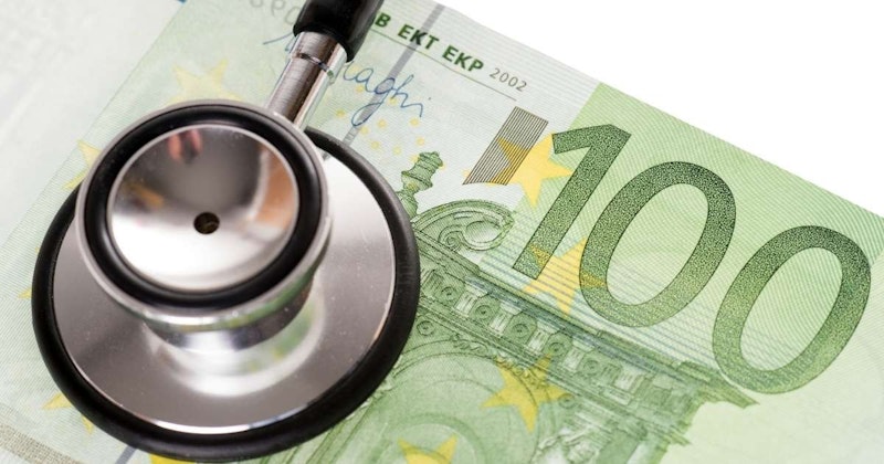 Bu görüntüde, vücudun iç seslerini dinlemek için kullanılan tıbbi bir cihaz olan stetoskop, bir para banknotu üzerinde yakın çekim olarak gösterilmektedir. Stetoskop metalden yapılmış olup gri ve sarı çizgilidir. Banknot net ve yenidir, köşesinde bazı yazılar görülebilmektedir. Banknot yeşil renktedir ve üzerinde küçük daireler ve dikdörtgenlerden oluşan bir desen vardır. Stetoskop, metal kafası faturanın kenarıyla hafifçe örtüşecek şekilde faturanın üzerinde nazikçe durmaktadır. Stetoskop hafifçe sağ tarafa doğru açılıdır ve çan şeklindeki ucu da aynı yöne bakmaktadır.