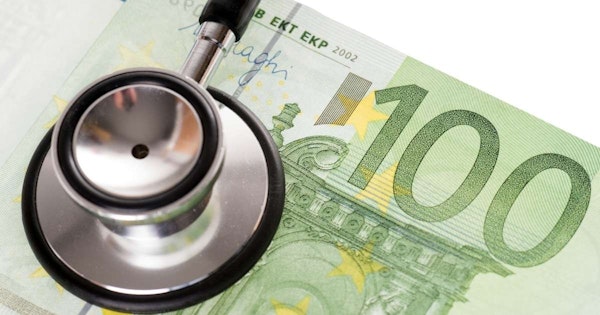 Bu görüntüde, vücudun iç seslerini dinlemek için kullanılan tıbbi bir cihaz olan stetoskop, bir para banknotu üzerinde yakın çekim olarak gösterilmektedir. Stetoskop metalden yapılmış olup gri ve sarı çizgilidir. Banknot net ve yenidir, köşesinde bazı yazılar görülebilmektedir. Banknot yeşil renktedir ve üzerinde küçük daireler ve dikdörtgenlerden oluşan bir desen vardır. Stetoskop, metal kafası faturanın kenarıyla hafifçe örtüşecek şekilde faturanın üzerinde nazikçe durmaktadır. Stetoskop hafifçe sağ tarafa doğru açılıdır ve çan şeklindeki ucu da aynı yöne bakmaktadır.