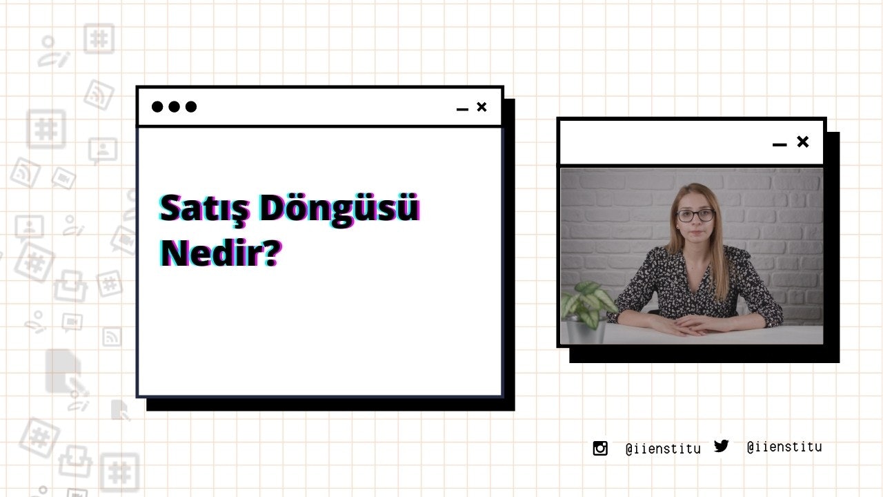 Bir kadın modern bir ofiste masasında oturuyor. Kollarını kavuşturmuş ve dümdüz ileriye bakıyor. Uzun, koyu renk saçları var ve siyah-mor bir gömlek giyiyor. Masanın üzerinde bir bilgisayar ve arka planda bir cep telefonunun ekran görüntüsü var. Sağında, her ikisi de hafifçe odak dışında kalan bir sebze ve bir bitki var. Solunda, üzerinde siyah ve kırmızı çizgiler olan beyaz bir kare ve bir bitkinin bulanık bir görüntüsü var.