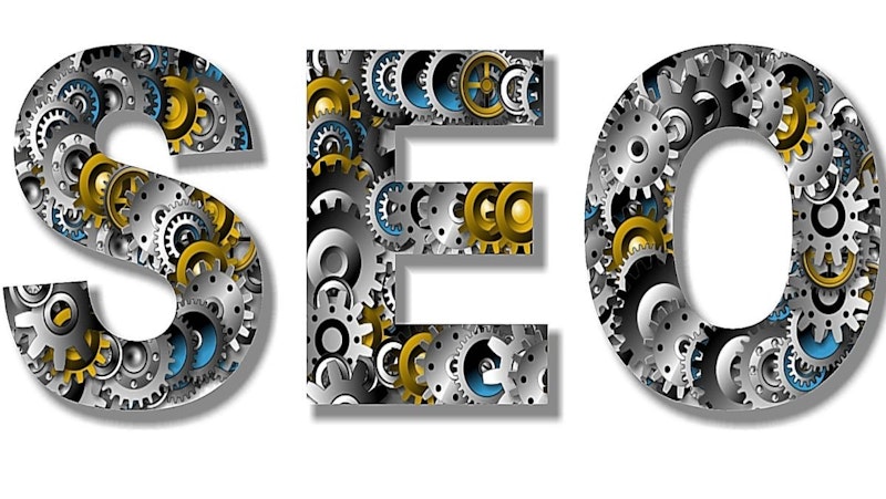 Birbirine bağlı dişlilerden oluşan bir O harfini sergileyen bir SEO veya arama motoru optimizasyonunun yakın çekimi. O, sarı ve siyah vurgularla ağırlıklı olarak beyazdır. O harfinin her iki yanında yine dişlilerden oluşan S ve E harfleri yer alıyor. Harfleri çevreleyen oval çerçeve beyaz renkli, sarı ve siyah kenarlıklı. Çerçeve harfleri çevrelemekte ve SEO'nun genel tasarımına katkıda bulunmaktadır.