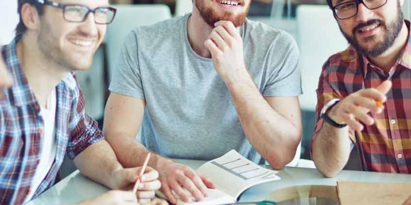 Bu resimde sakallı ve elinde bir kitap olan bir adam görülüyor. Ekose bir gömlek giyiyor ve bir grup başka erkekle birlikte bir masada oturuyor. Yüzü odaktadır ve gözleri doğrudan kameraya bakmaktadır. Sağ eli kitabı açık tutarken sol eli masanın kenarını kavramaktadır. Arkasında başka bir kişinin yüzünün bulanık bir görüntüsü var. Ön planda bir kağıt parçası tutan bir el var ve bu el hafifçe odak dışı. Görüntüdeki adamın ciddi bir ifadesi var, sanki kitaba konsantre olmuş gibi. Sakalı düzgünce kesilmiş ve gömleği düzgün ve temiz. Genel olarak, görüntü sakallı ve elinde kitap olan bir adamın yakın çekimidir.