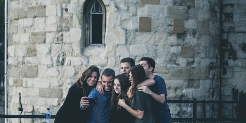 Bir grup insan sıcak, sevgi dolu bir kucaklaşmayla birbirlerini kucaklıyor. Kucaklaşma sıkı ve güçlü, fotoğraftaki insanlar arasındaki güçlü bağı vurguluyor. Bir kadın telefonuyla selfie çekerken, başka bir kadın da gruptaki bir erkeği kucaklıyor. Kadın ve erkek birbirlerine tatlı tatlı gülümsüyor ve anın tadını çıkarıyor gibi görünüyor. Adamın yüzüne yakın çekim yapıldığında, gözleri kapalı ve dudakları gülümseme şeklinde kıvrılmış bir şekilde memnun ifadesi ortaya çıkıyor. Arka planda siyah çerçeveli bir pencere ve köşede duran uzun saçlı bir kadın da var. Resimdeki tüm insanlar rahat kıyafetler giyiyor ve atmosfer rahat ve neşeli.