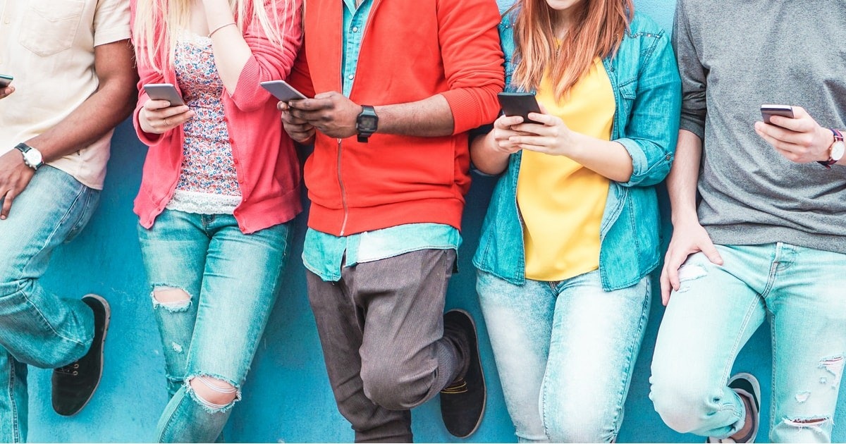 Bu görüntüde birbirine yakın duran beş kişilik bir grup görülüyor. Hepsinin elinde telefon var. En soldaki kişi pembe bir hırka ve yırtık kot pantolon giyen bir kadın. Onun yanındaki kişi kırmızı kazak ve gri pantolon giyen bir erkek. Ortada, beyaz gömlek ve mavi kot pantolon giyen başka bir kadın var. Yanındaki kişi sağ eliyle bir telefon tutuyor ve sol bileğine bir saat takıyor. Son kişi ise siyah gömlek ve yırtık kot pantolon giyen bir kadın. Tüm insanlar telefonlarına bakmaktadır. Resmin arka planı açık gri bir duvardır.