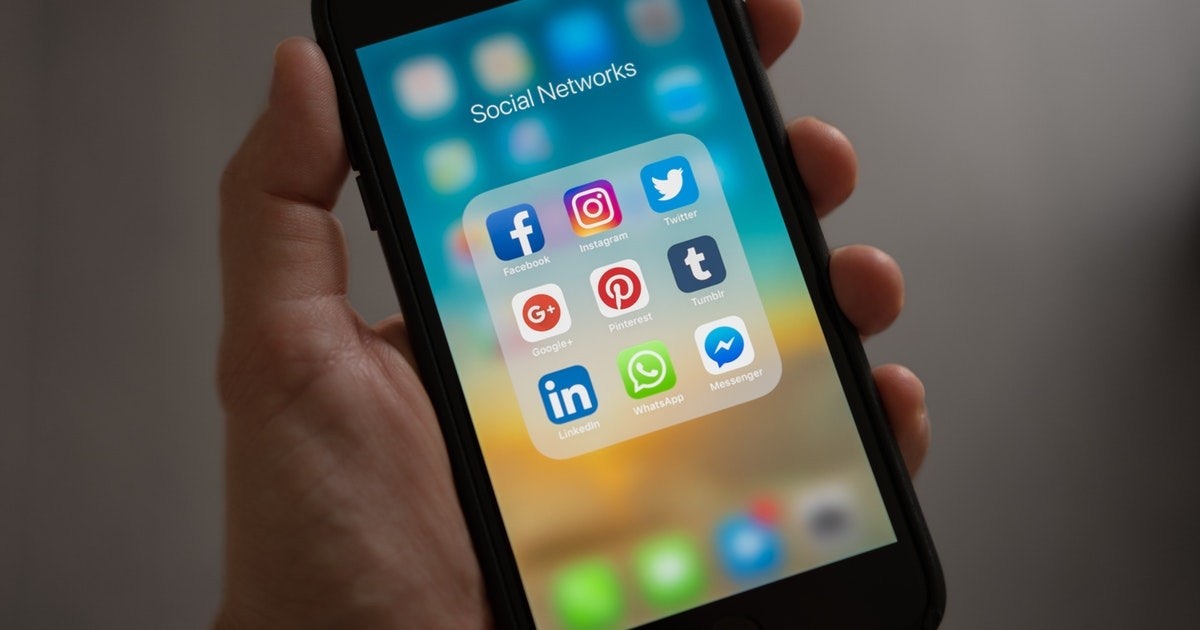 Bir kişi elinde siyah bir cep telefonu tutmaktadır. Telefonun ekranı aydınlatılmış ve üzerinde telefon, kamera, internet, saat ve müzik notası gibi çok sayıda simge var. Telefon dik bir pozisyonda tutulmakta ve kişinin başparmağı telefonun alt kısmına dayanmaktadır. Kişinin diğer parmakları telefonun etrafına sarılmış ve kavramayı sağlamaktadır. Kişi dikkatle telefon ekranına bakmakta ve simgelere odaklanmaktadır.