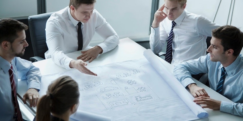 Bir grup insan bir masanın etrafında toplanmış, dikkatle bir plana bakmaktadır. Masanın başında beyaz gömlekli ve kravatlı bir adam oturuyor, elinde bir kalem var ve önündeki kâğıdı inceliyor. Sağında at kuyruklu bir kadın oturuyor, gözleri belgeye odaklanmış. Yan tarafta, beyaz gömlekli ve kravatlı bir başka adam, kravatın yakın çekimiyle yüzü kısmen gizlenmiştir. Grup, gözleri kâğıt ve birbirleri arasında gidip gelerek planın içeriğini tartışmaya devam ediyor. Konuşmaya dalmışlar, karar vermek için belgenin sağladığı bilgileri kullanıyorlar.