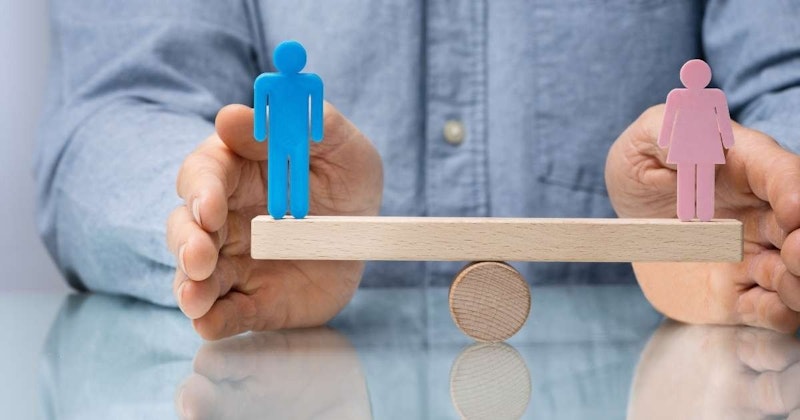 Bir kişi ahşap bir yüzey üzerinde küçük, mavi bir heykelciği dengede tutarken görülüyor. Kişi çerçevenin ortasında durmakta, kollarını açmış ve gözlerini aşağıya dikerek dikkatini heykelciğe odaklamaktadır. Ahşap yüzey, heykelciği çevreleyen dairesel bir desene sahip ve arka planda pembe kağıttan bir kadın kesiti de görülüyor. Heykelciğin altındaki kum yüzeyin yakın çekimi sahneye daha da katkıda bulunuyor. Arka plandaki masa da genel görüntüye katkıda bulunarak güzel ve ayrıntılı bir görsel oluşturuyor.