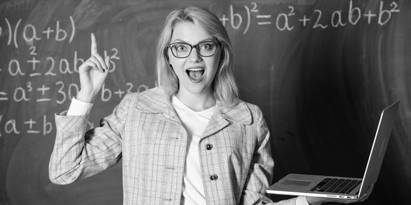 Gözlüklü bir kadın, elinde bir dizüstü bilgisayar ve bir kitap tutarak kara tahtanın önünde durmaktadır. Ağzı hafifçe açık bir şekilde doğrudan kameraya bakmaktadır ve gözleri gözlükleriyle çerçevelenmiştir. Üzerinde ekose bir ceket vardır ve parmağıyla yukarıyı işaret etmektedir. Arkasındaki kara tahta beyaz yazılar ve denklemlerle doludur. Elindeki dizüstü bilgisayar gümüş, kitap ise koyu kırmızı renktedir. Kadın açık mavi bir arka planla çevrelenmiştir.