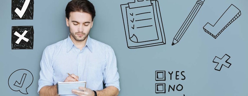 Kahverengi saçlı ve sakallı bir adam oturmuş bir deftere bir şeyler yazmaktadır. Beyaz uzun kollu bir gömlek giyiyor ve önünde bir kontrol listesi bulunan bir pano var. Panoda, siyah kenarlıklı siyah beyaz bir kare ve içinde beyaz bir onay işareti var. Defterde, bir konuşma balonunun içinde siyah bir onay işareti vardır. Defterin solunda, siyah bir karenin içinde beyaz bir çarpı işareti var. Adamın yüzünde ciddi bir ifade var ve elleri odakta, yakın çekimle görülebiliyor.