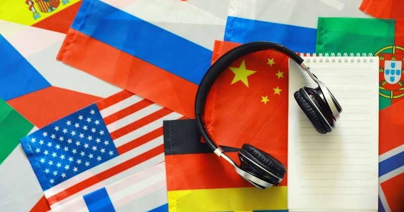 Bu görüntü, kırmızı beyaz çizgili bir bayrakla kaplı bir masanın üzerinde duran bir çift kulaklığı gösteriyor. Ön planda, ortasında sarı bir yıldız bulunan bayrağın yakın çekimi görülebiliyor. En sağda, kulaklıklar bir not defterinin üzerinde dururken görülüyor ve kulaklıkların yakın çekimi de görülebiliyor. Arka planda, üzerinde bazı metinler bulunan sarı ve kırmızı bir işaret görülmektedir. Bu görsel, ders çalışırken müzik dinleme ya da sadece huzur ve sessizliğin tadını çıkarma fikrini temsil etmek için kullanılabilir.