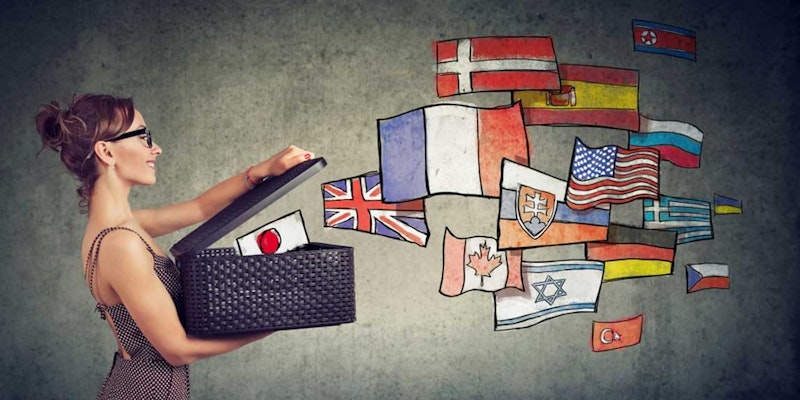 Bir kişi, içinden çeşitli renk ve desenlerde bayraklar çıkan bir kutuyu açıyor. Kişinin üzerinde siyah uzun kollu bir gömlek var ve kutuyu iki eliyle tutuyor. Sol kolunu da bir bilgisayarın üzerine uzatmıştır. Ön planda açık kahverengi tenli ve siyah uzun kollu gömlekli bir kadının kolunun yakın çekimi görülüyor. Kol, siyah dikdörtgen bir nesne tutmaktadır. Kutunun içindeki bayraklar farklı boyutlarda ve tasarımlarda görünüyor. Bayrakların renkleri kırmızı, sarı, mavi, yeşil ve beyazdır.