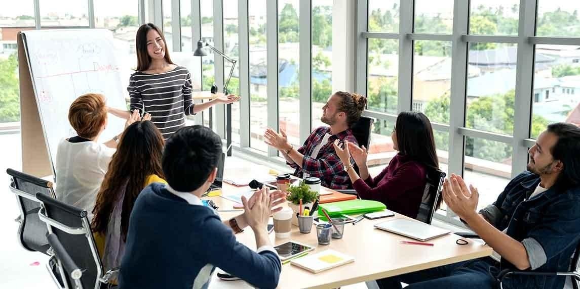 Çizgili gömlekli bir kadın bir grup insanın önünde durmuş alkış tutmaktadır. Bir grup insan bir masanın etrafında oturmaktadır ve kadın odanın ortasındadır. Gülümsemekte ve odaya bakmaktadır. Kadının sağında alkışlayan tekerlekli sandalyeli bir adam ve solunda alkışlayan tekerlekli sandalyesiz bir adam vardır. Grubun arkasında dışarıyı gören bir pencere vardır. Grubun önündeki masanın üzerinde içinde sarı bir sıvı olan beyaz bir tabak vardır.