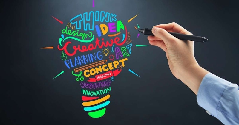 Soluk mavi kollu, siyah bir kalem tutan bir elin yakın çekimi. Kalemin üstünde sarı bir ok var ve elin parmakları kalemi sıkıca kavrarken görülüyor. El, bilekten parmak eklemlerinin hemen altına kadar görülüyor ve kalem ortada yer alıyor. Görüntünün arka planı bulanık ve odak dışıdır. El açık gri bir arka plan üzerine yerleştirilmiştir.