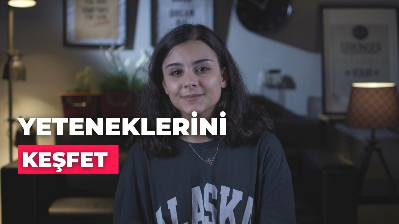 Bu resim yüzünde inanılmaz mutlu bir ifade olan bir kadını gösteriyor. Gözleri kapalı ve ağzı hafifçe açık, genişçe gülümsüyor. Saçları açık kahverengi ve düzgünce şekillendirilmiş. Kısa kollu beyaz bir gömlek ve mavi bir etek giyiyor. Resmin arka planı bulanık ama ahşap zeminli ve açık renkli duvarlı bir oda gibi görünüyor. Resmin sol tarafında bir abajur ve sağ taraftaki masanın üzerinde küçük bir bitki var. Kadın odanın ortasında durmuş, kendinden emin ve neşeli bir şekilde kameraya bakıyor. Saf bir mutluluk hali içinde görünüyor.