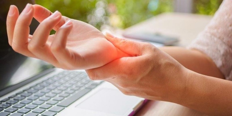 Resimde uzun, siyah saçlı, beyaz gömlekli bir kişi görülüyor. Sol eliyle bileğini tutmakta ve bileğine bakmaktadır. Sağ elini hafifçe kaldırmış ve klavyenin yan tarafına bastırmış. Kişi derin düşüncelere dalmış ve önündeki işe odaklanmış gibi görünüyor. İfadelerinde bir konsantrasyon belirtisi var. Oda iyi aydınlatılmış ve duvarlar açık griye boyanmış. Klavye orta büyüklükte, gümüş renkli ve birkaç tuşu parlak sarı renkle vurgulanmış.