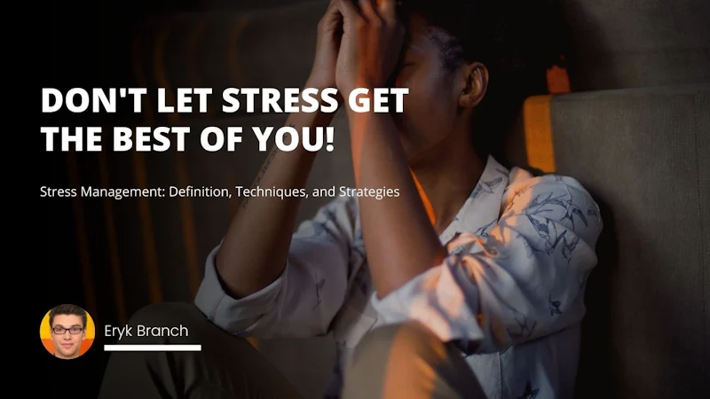 A woman is sitting on a couch with her hands in her face, appearing to be in a state of distress. She is wearing a white shirt and black pants, and has her dark hair pulled back away from her face. Her eyes are closed and her mouth is slightly open. She has glasses on and is leaning forward with her elbows resting on her knees. Behind her is a black and white o-shaped sign on a wall. The room is lit with a warm yellow light. She appears to be alone in her thoughts, in a moment of reflection and contemplation.
