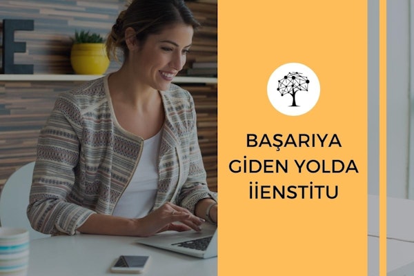 Genç bir kadın masa başında oturmuş, dizüstü bilgisayarına bakarken gülümsüyor. Uzun açık kahverengi saçları yüzünden geriye doğru toplanmış. Üzerinde beyaz düğmeli bir gömlek var ve elleri dizüstü bilgisayarın klavyesinde. Arkasında, içinde yeşil bir bitki olan sarı bir saksı görülüyor. Görüntünün en sağ tarafında bulanık mavi ve beyaz çizgili bir nesne var. Resmin alt kısmında, ön planda bir eli dizüstü bilgisayarın üzerinde olan bir kişinin kafasının yakın çekimi yer alıyor. Kişinin dikey çizgili bir desene sahip gömleği de görüntüde görülebiliyor.