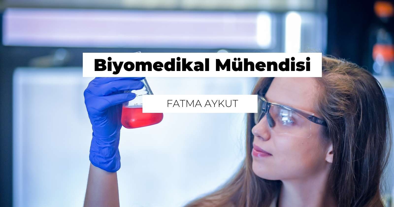 Bu resimde koruyucu gözlük ve eldiven takmış bir kadın, kırmızı sıvıyla dolu bir test tüpünü tutarken görülüyor. Kadın resmin ortasında, beyaz bir laboratuvar önlüğü ve mavi çiçek desenli bir gömlek giyiyor. Konsantrasyon ve odaklanma ifadesiyle doğrudan kameraya bakıyor. Test tüpünü sağ elinde sıkıca tutuyor, sol eli eldivenli ve daha fazla denge sağlamak için tüpün yan tarafına dayanmış durumda. Test tüpü şeffaftır ve içindeki kırmızı sıvının görünmesini sağlar. Arka planda bir logo ve bir dizi başka laboratuvar ekipmanı görülüyor.