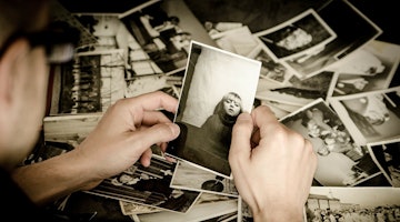 Beyaz elbise giyen bir kişi, kameranın çekebilmesi için gülümseyen bir çocuğun fotoğrafını tutuyor. Fotoğraftaki çocuk mavi bir tişört giymektedir ve yüzünde parlak bir gülümseme vardır. Fotoğrafı tutan kişi diğer elini kalçasına koymuş ve doğrudan kameraya bakmaktadır. Fotoğraf yakın plandan çekilmiş, odak noktası kişi ve tuttuğu fotoğraf. Arka plan bulanıktır ve arka planda bir yığın başka fotoğraf görülebilir. Ayrıca, görüntünün sağ alt köşesinde bulanık bir tekerlek görülebiliyor.