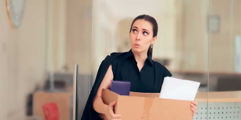 Bir kadın içi eşya dolu büyük bir kutu taşımaktadır. Açık renkli bir gömlek ve koyu renkli bir pantolon giyiyor. Saçları at kuyruğu şeklinde arkaya toplanmış. Yüzünde kararlı bir ifadeyle yana doğru bakıyor. Kutunun içinde kağıtlar, kutular ve diğer nesneler de dahil olmak üzere çeşitli eşyalar var. Kutu vücudundan biraz daha büyüktür ve iki eliyle tutmaktadır. Arka planda, üzerinde siyah kareler olan bir beyaz tahta görülüyor. Kadın acelesi varmış gibi görünüyor, sanki önemli bir yere gidiyormuş gibi. Yürürken kutunun elinde güvenli bir şekilde tutulduğundan emin oluyor.