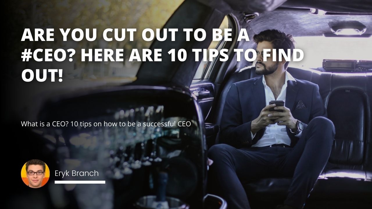 A man in a suit is sitting in the back of a black limousine. He is looking at his phone and wearing glasses. He has a beard and a moustache. His hands are resting on his lap, and he is looking intently at his phone. There is a group of beer glasses in the foreground of the image, with a white letter 'O' amongst them. In the background of the image, there is a close-up of a seat in the car.