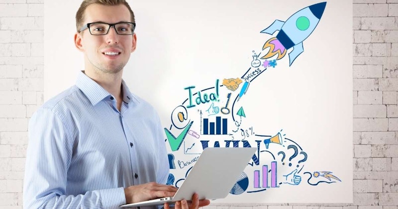 Gözlüklü ve dizüstü bilgisayarlı bir adam beyaz tuğla bir duvarın önünde duruyor. Yüzünde bir gülümsemeyle doğrudan kameraya bakmaktadır. Dizüstü bilgisayarı açık ve iki eliyle tutuyor. Arka planda, duvara çizilmiş parlak turuncu alevli bir roket karikatürü var. Adam koyu yeşil bir gömlek giyiyor ve kısa, siyah saçları var. Teni hafifçe bronzlaşmış. Ayaklarını hafifçe açmış ve kollarını hafifçe bükmüş bir şekilde rahat bir pozda durmaktadır.