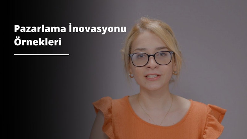 Gözlüklü bir kadın kameraya sıcak bir ifadeyle bakıyor. Parlak turuncu uzun kollu bir gömlek giyiyor ve siyah saçları yüzünden geriye doğru toplanmış. Gözlükleri gümüş desenli yuvarlaktır ve boynunda zarif bir altın kolye vardır. Beyaz bir duvarın önünde duruyor, elleri yanlarında duruyor. Gözleri kahverengi ve dudakları sanki bir şey söylemek üzereymiş gibi hafifçe ayrık. Kendinden emin ve dingin görünüyor ve görüntü bir sakinlik ve güç hissi veriyor.