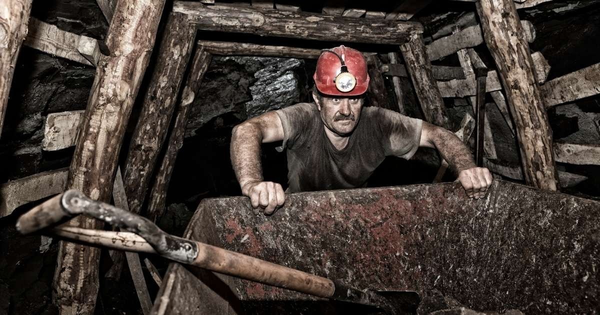 Kask ve parlak kırmızı baret takmış bir adam resmin ön planında duruyor. Sol elinde uzun beyaz bir kiriş tutarken sağ yumruğunu sıkıca sıkmış. Yüzü yakın plandadır ve çerçevenin hafifçe soluna bakmaktadır. Miğferi beyazdır ve üzerinde bir ışık varmış gibi görünmektedir. Resmin arka planında taş bir duvar ve sağ alt köşede kısmen görülebilen bir kürek var. Adamın etrafı gölgelerle çevrili, bu da parlak kırmızı baretin daha da öne çıkmasını sağlıyor. Resim güç ve kararlılığın mükemmel bir örneği.