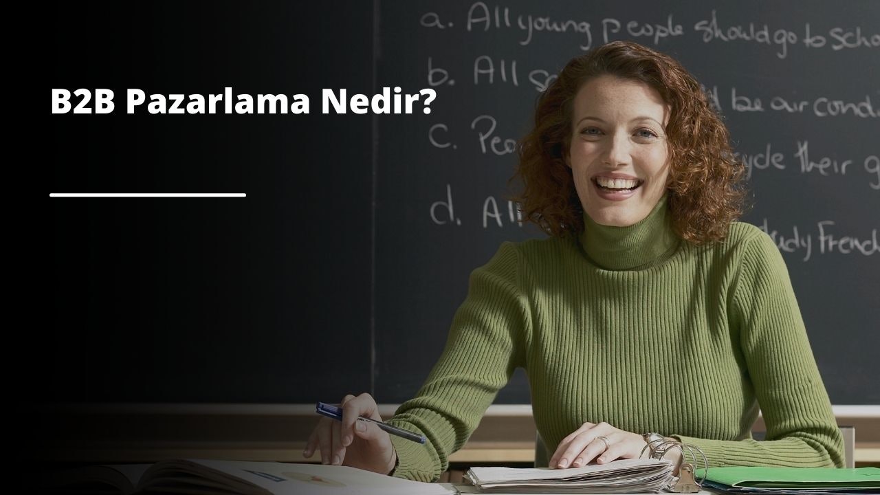 Yüzü sıcak bir ışıltıyla aydınlanmış bir kadın kameraya gülümsüyor. Bir masada oturmaktadır ve yanındaki gazete yığınının üzerinde siyah beyaz bir logo basılıdır. Sağ elinde bir kalem tutuyor ve solundaki masanın üzerinde duran kağıt yığınına doğru tutuyor. Yüzü yakın plandadır, sırıtışı geniş ve davetkârdır. O anda mutlu ve memnun görünüyor, gözleri sevinçle parıldıyor. Arkasında, bir eli gazete yığınının üzerinde duruyor ve rahat atmosferi daha da belirginleştiriyor. Bu, memnuniyet ve neşe dolu, sıcak ve mutlu bir görüntü.