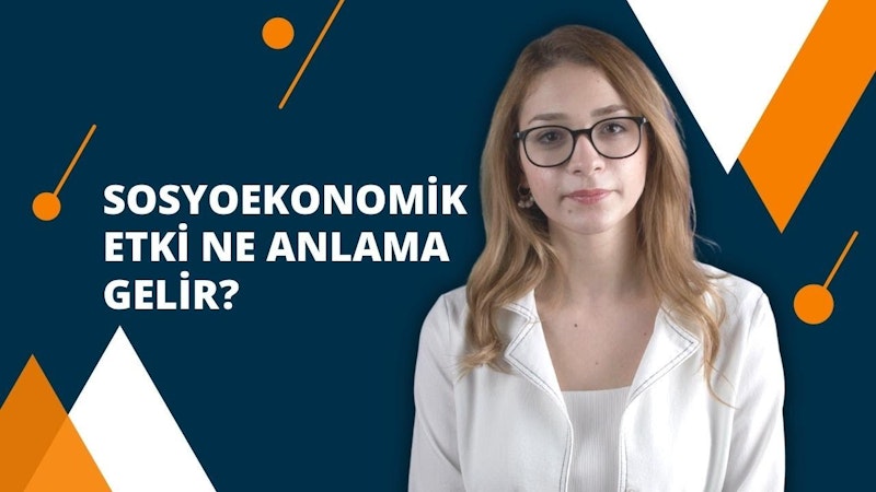Bir kadın beyaz bir gömlek ve gözlük takıyor. Uzun, koyu kahverengi saçları var ve gözleri gözlüklerin arkasından görünüyor. Gözlük ince, siyah bir çerçeveye sahip ve camları hafifçe renklendirilmiş. Beyaz gömleğin sol tarafında küçük turuncu bir daire var. Kadın doğrudan kameraya bakıyor, ifadesi odaklanmış ve niyetli. Arka plan koyu, parlak bir mavidir ve sol üst köşede beyaz bir metin yazılıdır. Görüntü kadının yüzünün ve göğsünün yakın çekimidir, gözleri ve gömleği çerçevenin büyük kısmını kaplamaktadır. Işık yumuşaktır ve kadının yüz hatlarını vurgulayarak görüntüye doğal ve davetkar bir görünüm kazandırır.