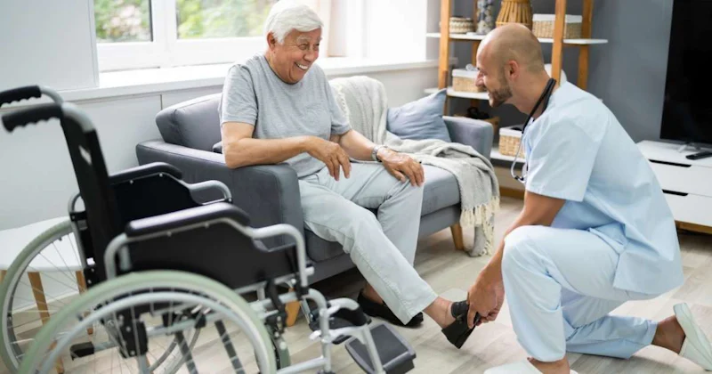 İki adam bir kanepede oturmuş, birbirlerine bakıyor ve gülümsüyorlar. Soldaki adam beyaz bir gömlek giyiyor ve sakallı. Sağdaki adam ise mavi bir önlük giymiş ve yere diz çökmüş. Arkalarında içinde bir kadın olan bir tekerlekli sandalye var. Arka planda, beyaz olabilecek gibi görünen bulanık bir nesne var. Her iki adam da mutlu ve memnun görünüyor, birbirlerinin arkadaşlığından keyif alıyorlar.