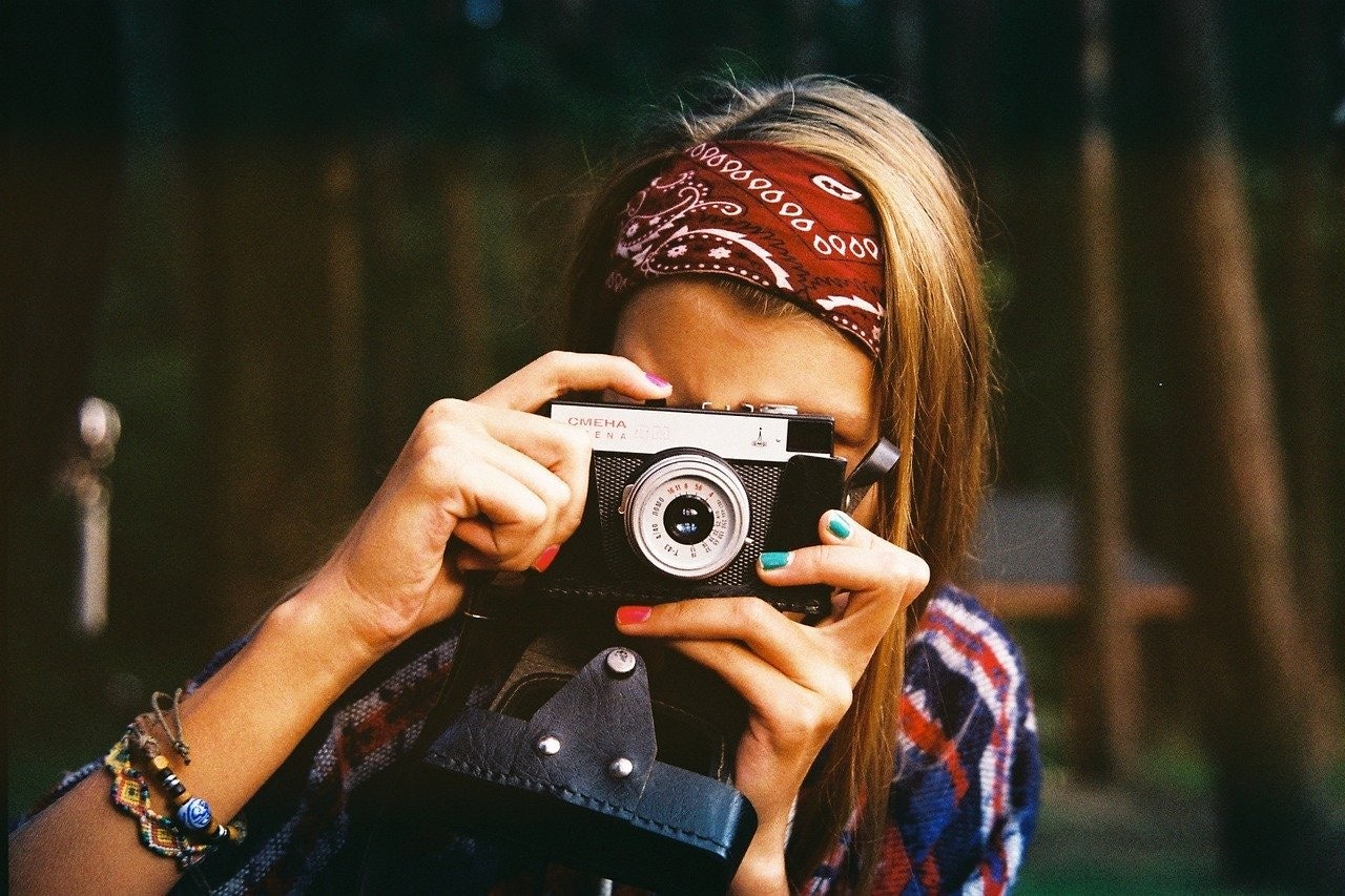 Başına lacivert bir bandana sarmış ve gümüş bir kolye takmış bir kadın görülüyor. Elinde bir fotoğraf makinesi tutuyor ve siyah deri bir kayış vücudundan geçiyor. Bakışları doğrudan kadraja yakın olan kamera objektifine yönelmiştir. Sol elini kameranın üst kısmına, sağ elini de yan tarafına koymuş. İfadesi ciddi ve odaklanmış. Arka plan odak dışıdır, bu da fotoğraftaki kamera ve kadın vurgusuna katkıda bulunur.