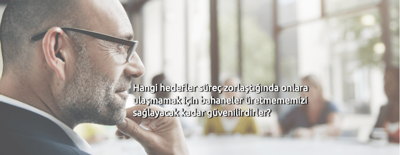 Bu, gözlüklü ve eli çenesinde olan bir adamın yakın çekim görüntüsüdür. Sakallı ve gözleri hafifçe odak dışında. Başı hafifçe eğiktir ve dudakları hafifçe ayrılmıştır. Üzerinde koyu renk bir ceket, altında açık renkli bir gömlek ve gri bir kravat var. Yüzünde ciddi ve düşünceli bir ifade var. Derin düşüncelere dalmış ya da bir iç gözlem anında kaybolmuş olabilir. Arka planda görüntünün atmosferine katkıda bulunan ince bir bulanıklık var.